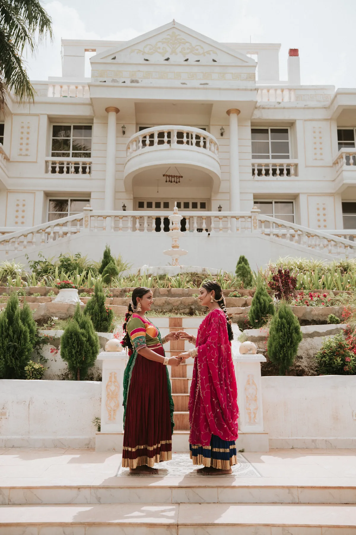 Two women modelling traditional outfits in front of a white building